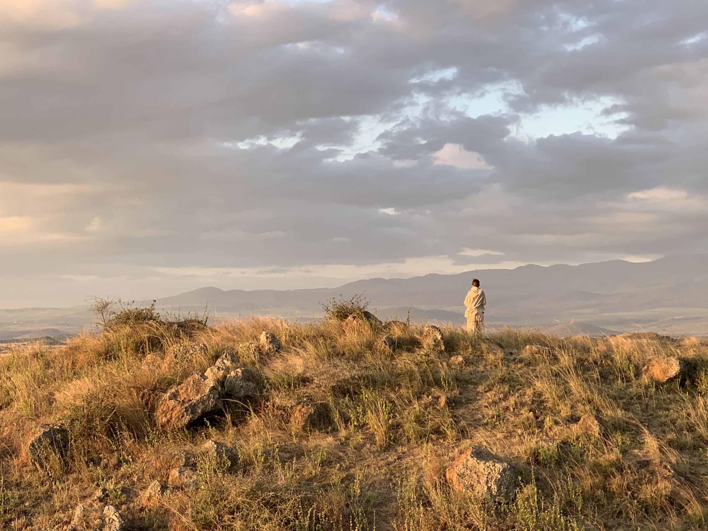 A lone figure in stillness on a ridge above the plains at dusk